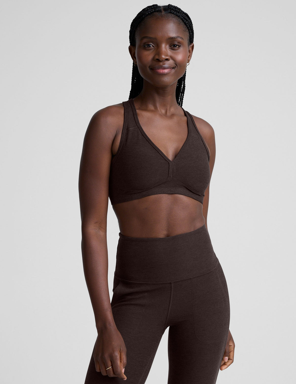 woman wearing a brown v-neck sports bra and pants on a plain background.