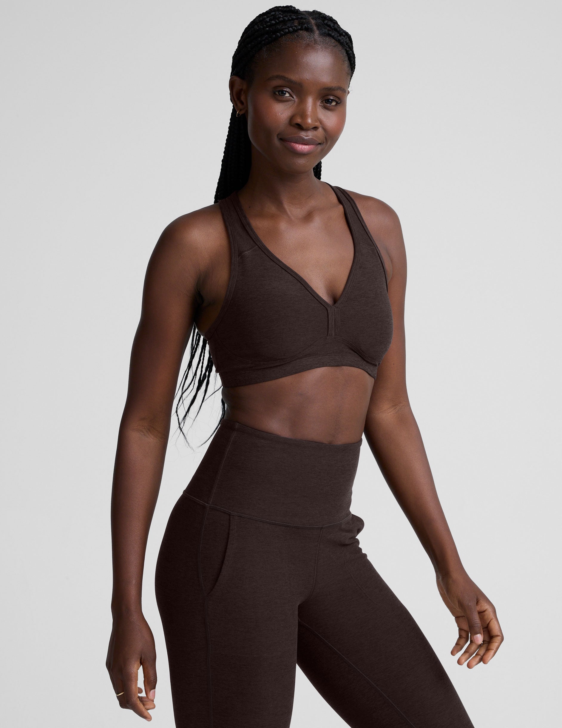 woman wearing a brown v-neck sports bra and pants on a plain background.