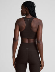 woman wearing a brown v-neck sports bra and pants on a plain background.