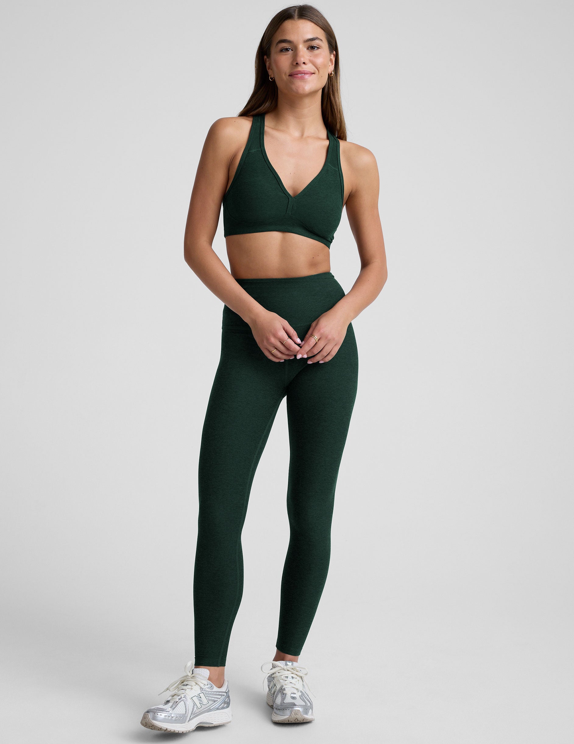 woman wearing a green sports bra and leggings on a light gray background.
