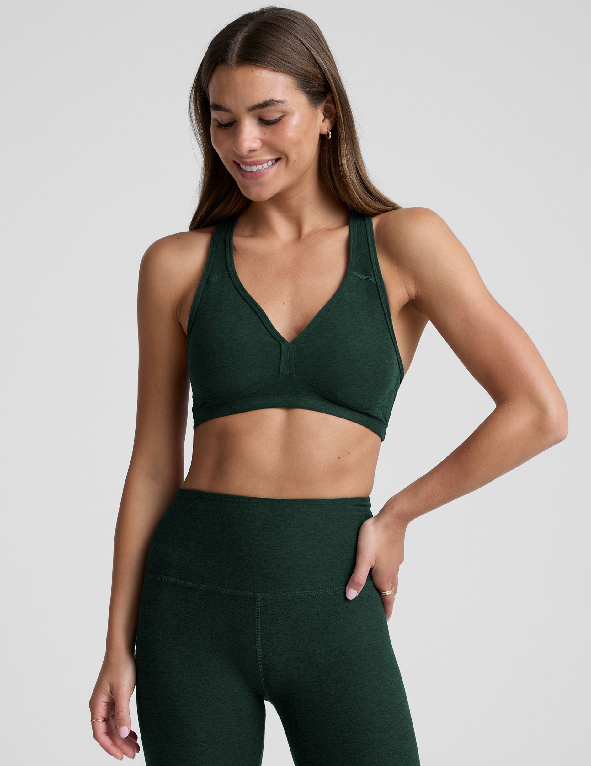 woman wearing a green sports bra and leggings on a light gray background.
