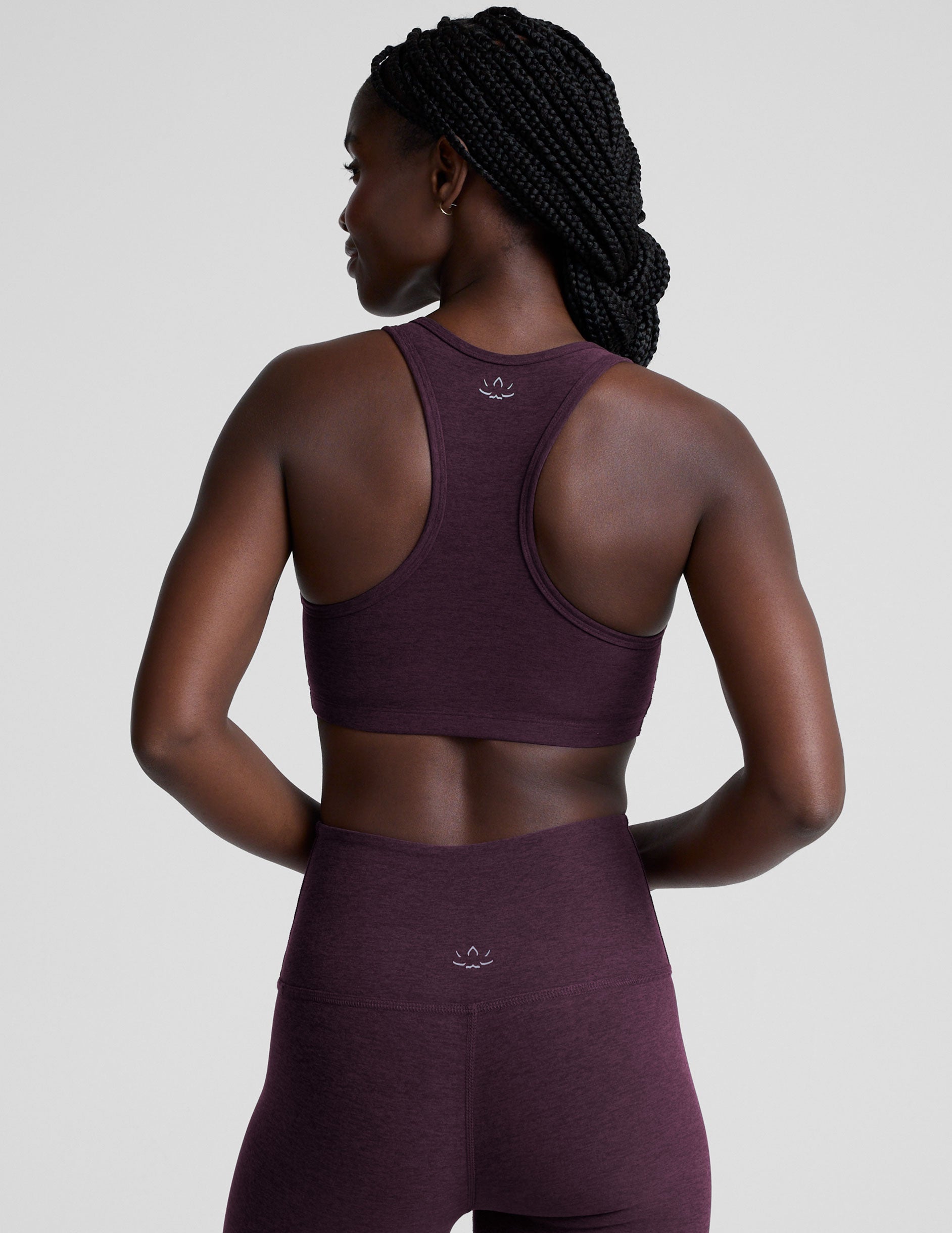 model wearing a purple soft v-neck racerback sports bra and leggings on a plain background.