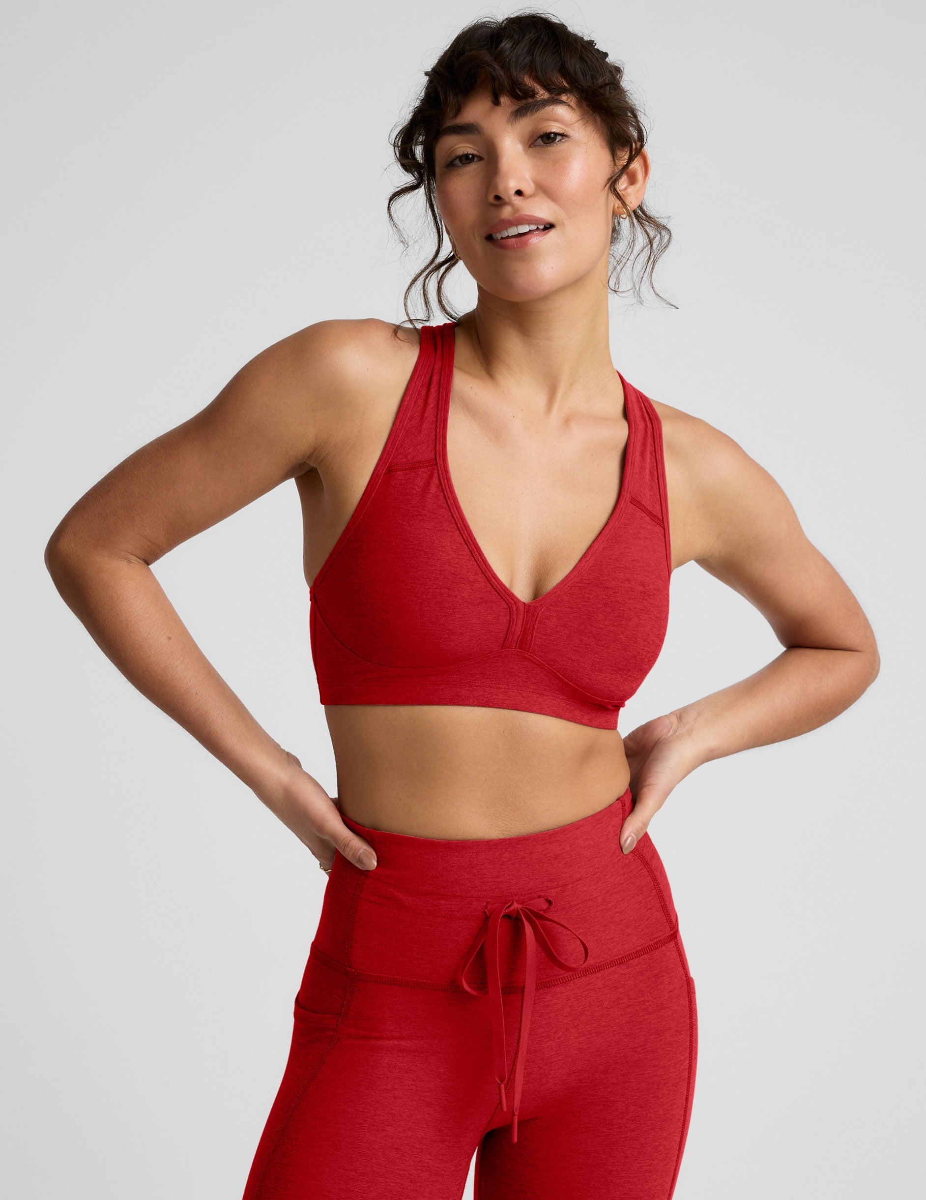 Woman wearing a red v-neck bra and leggings on a light background.