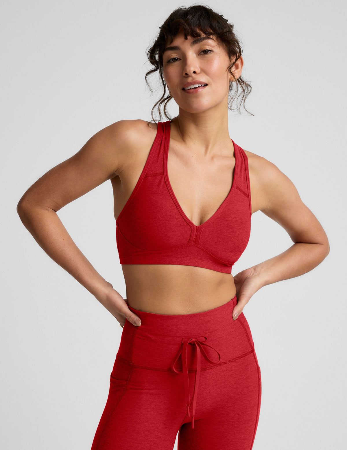 Woman wearing a red v-neck bra and leggings on a light background.