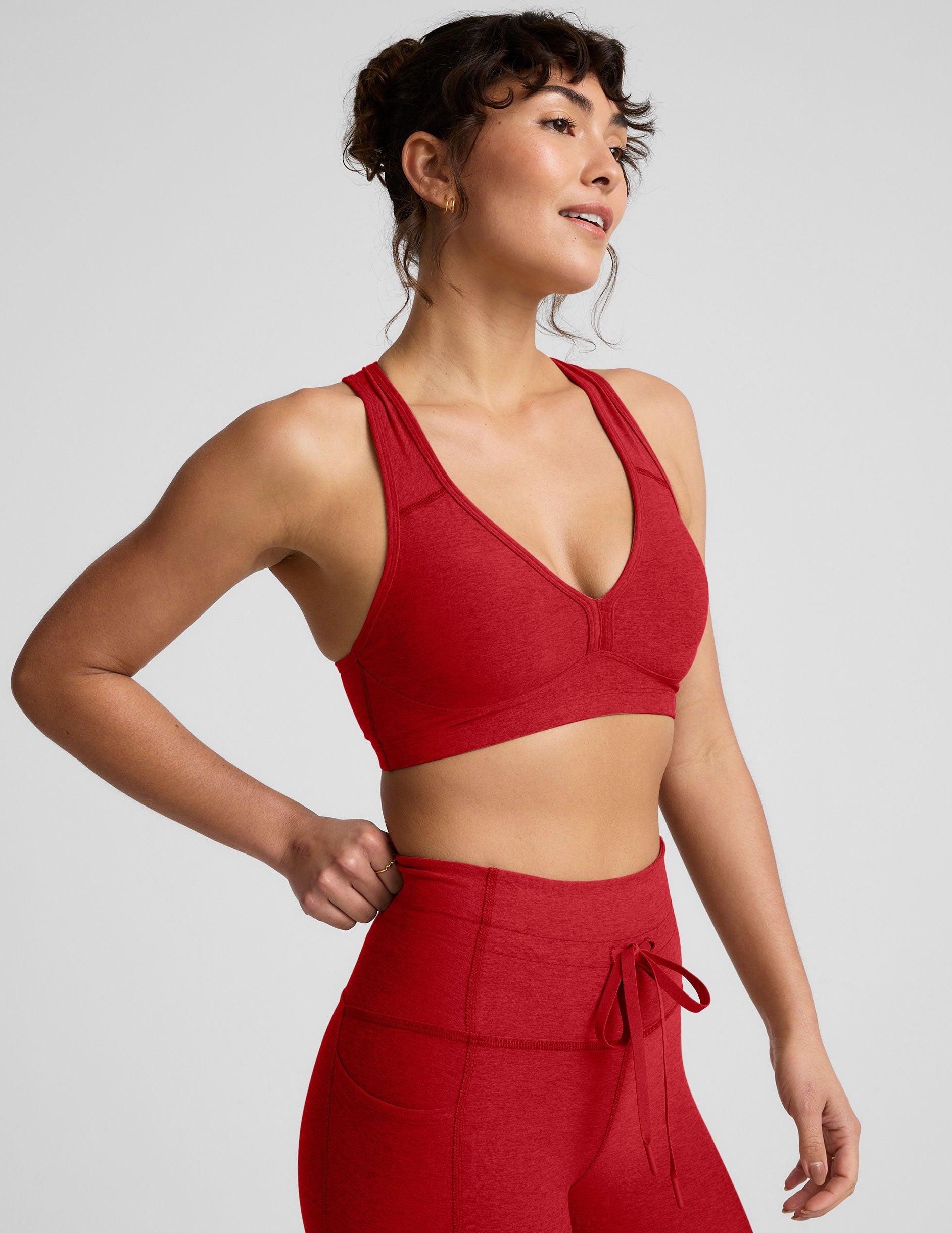 Woman wearing a red v-neck bra and leggings on a light background.