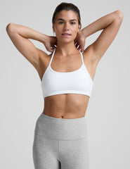 woman wearing a white slim racerback sports bra and gray leggings on a plain background.