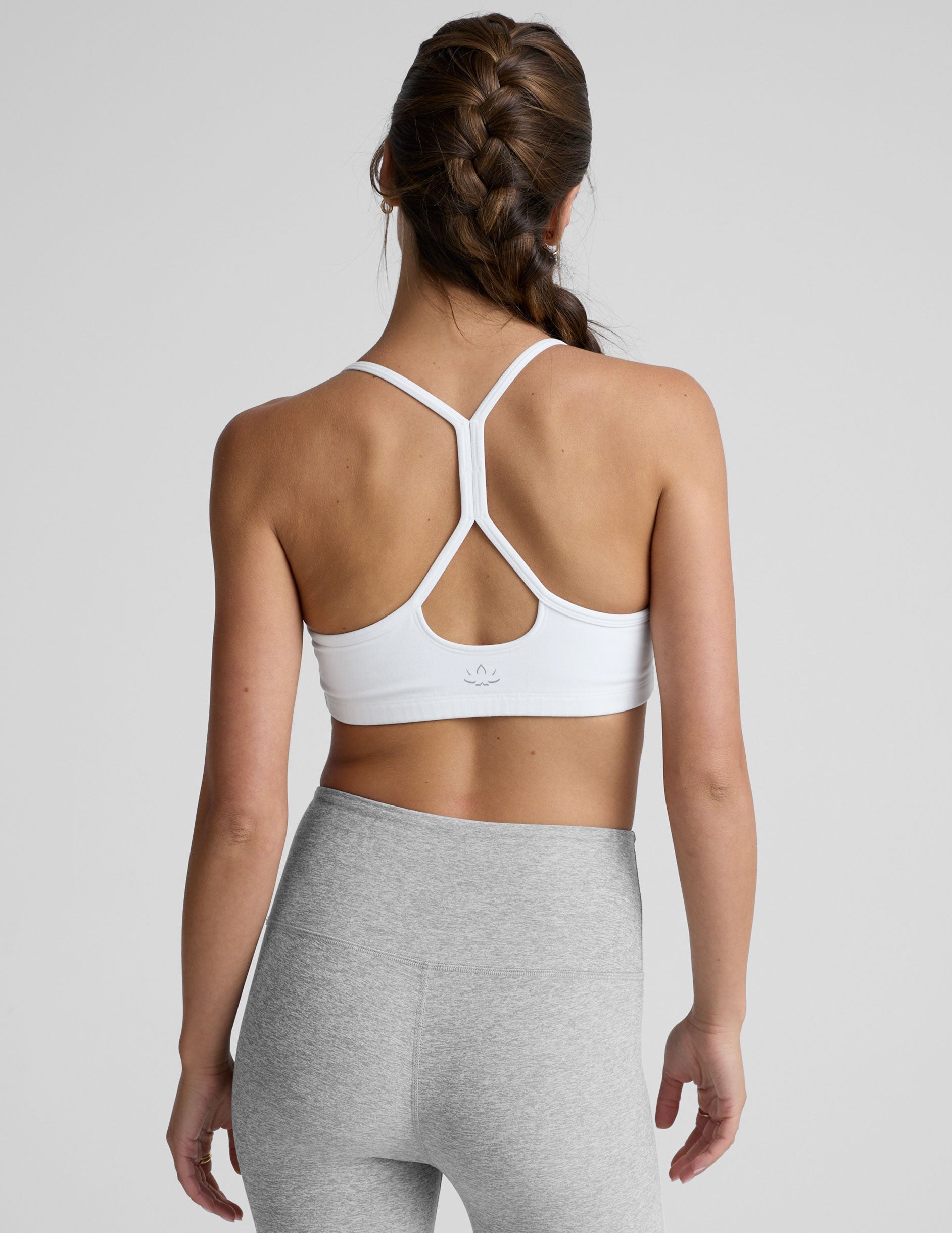 woman wearing a white slim racerback sports bra and gray leggings on a plain background.
