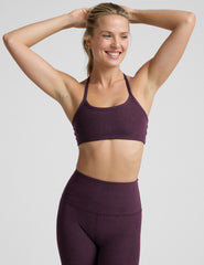 model wearing a purple slim strapped racerback bra and leggings on a light gray background.
