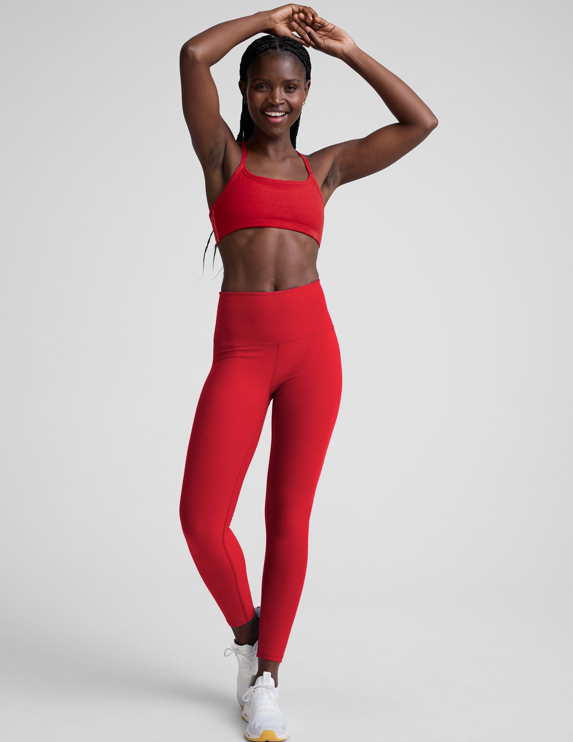 Woman wearing a red sports bra and leggings on a light background.