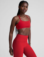 Woman wearing a red sports bra and leggings on a light background.