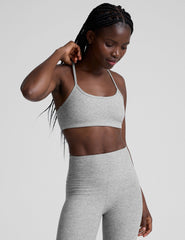 model is wearing a gray racerback bra with slim spaghetti straps and leggings against a plain background.