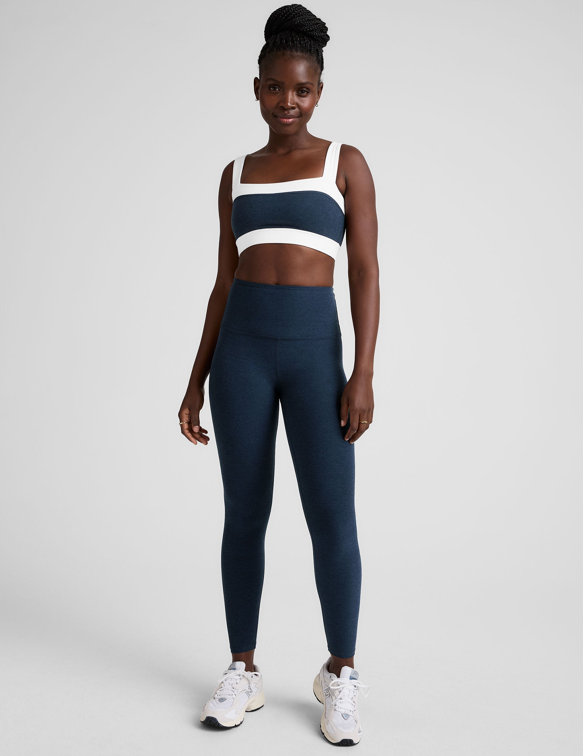 model is wearing a blue square neck bra with white horizontal colorblock stripe panels and a blue high-waisted midi length leggings.