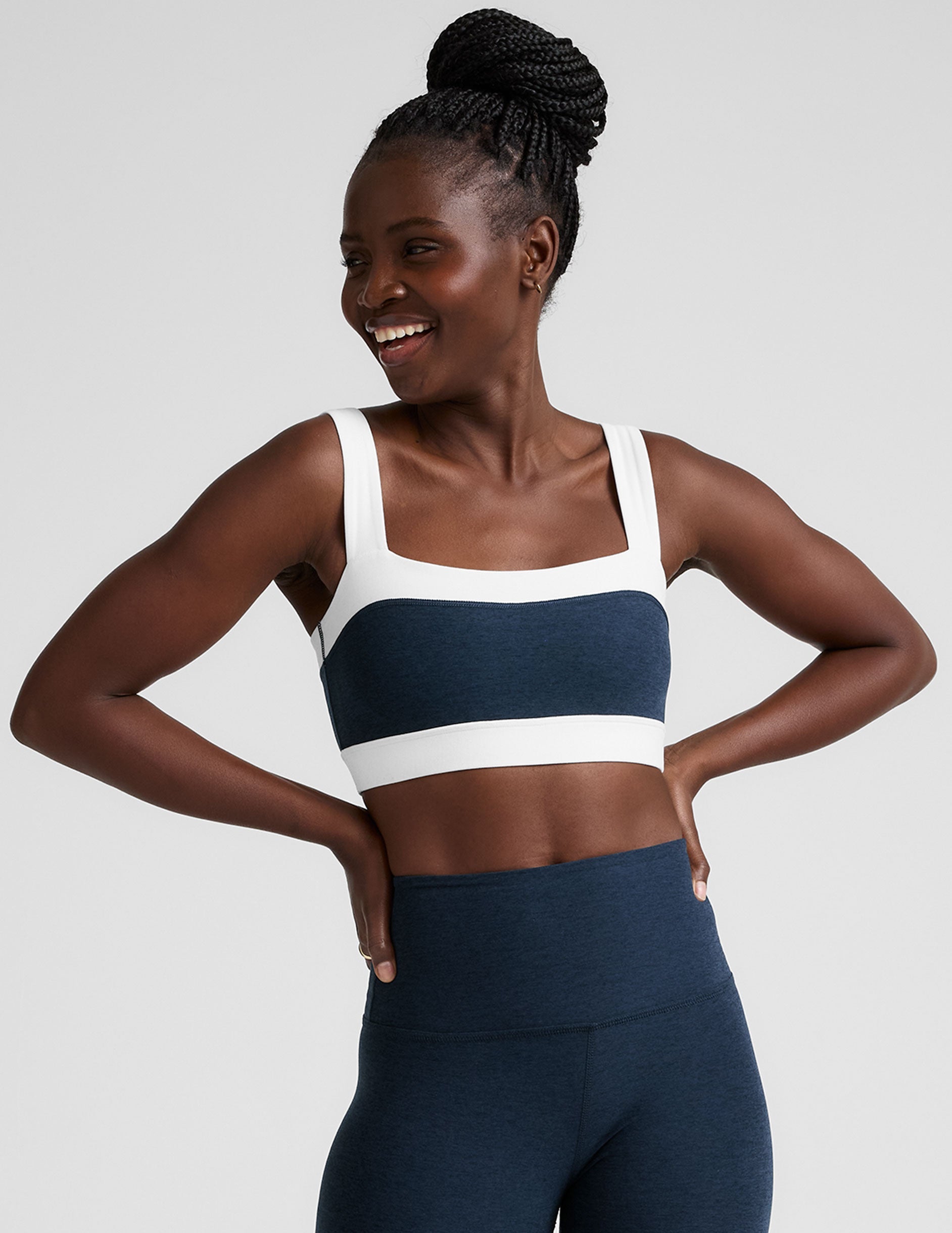 model is wearing a blue square neck bra with white horizontal colorblock stripe panels and a blue high-waisted midi length leggings.