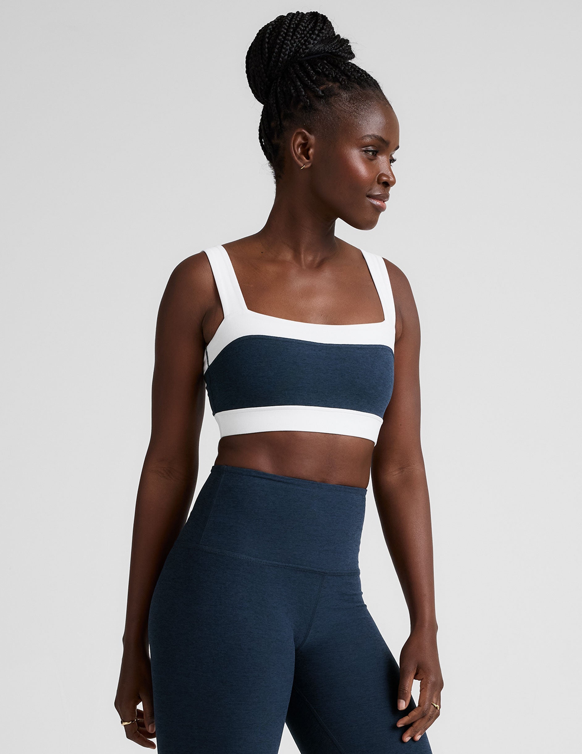 model is wearing a blue square neck bra with white horizontal colorblock stripe panels and a blue high-waisted midi length leggings.