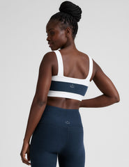 model is wearing a blue square neck bra with white horizontal colorblock stripe panels and a blue high-waisted midi length leggings.