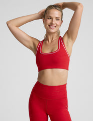 Woman wearing a red sports bra and leggings with white piping on a light background.