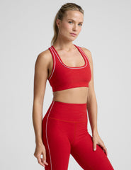 Woman wearing a red sports bra and leggings with white piping on a light background.