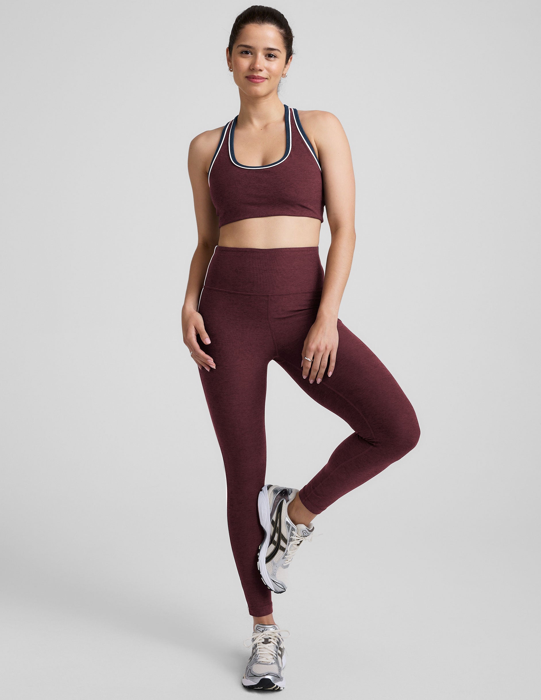 model wearing a maroon sports bra and leggings set on a gray background.