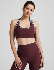 model wearing a maroon sports bra and leggings set on a gray background.