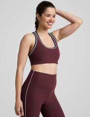 model wearing a maroon sports bra and leggings set on a gray background.
