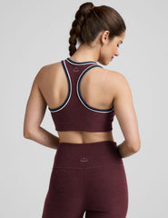 model wearing a maroon sports bra and leggings set on a gray background.