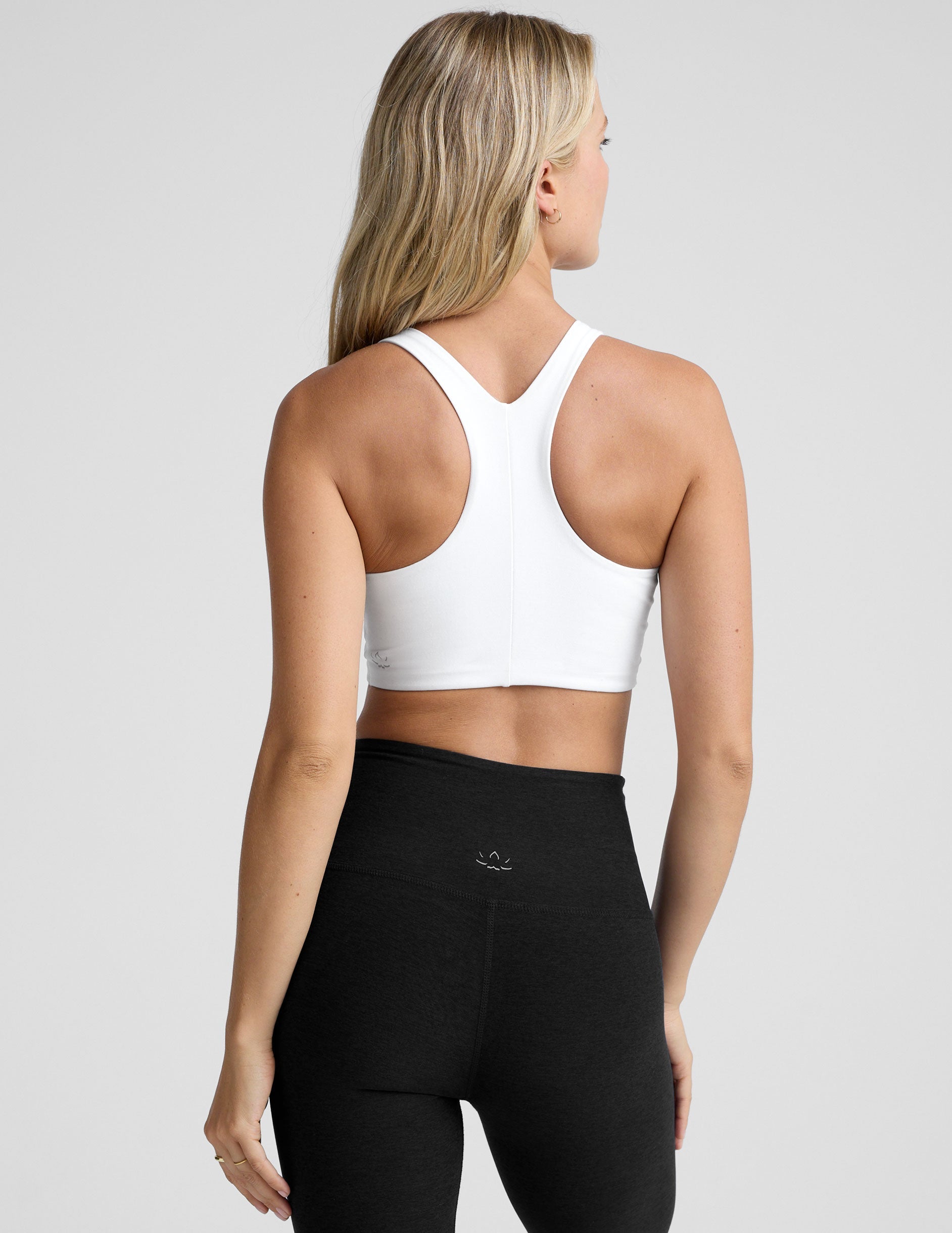 model wearing a white high-neck racerback sports bra and black leggings on a light gray background.