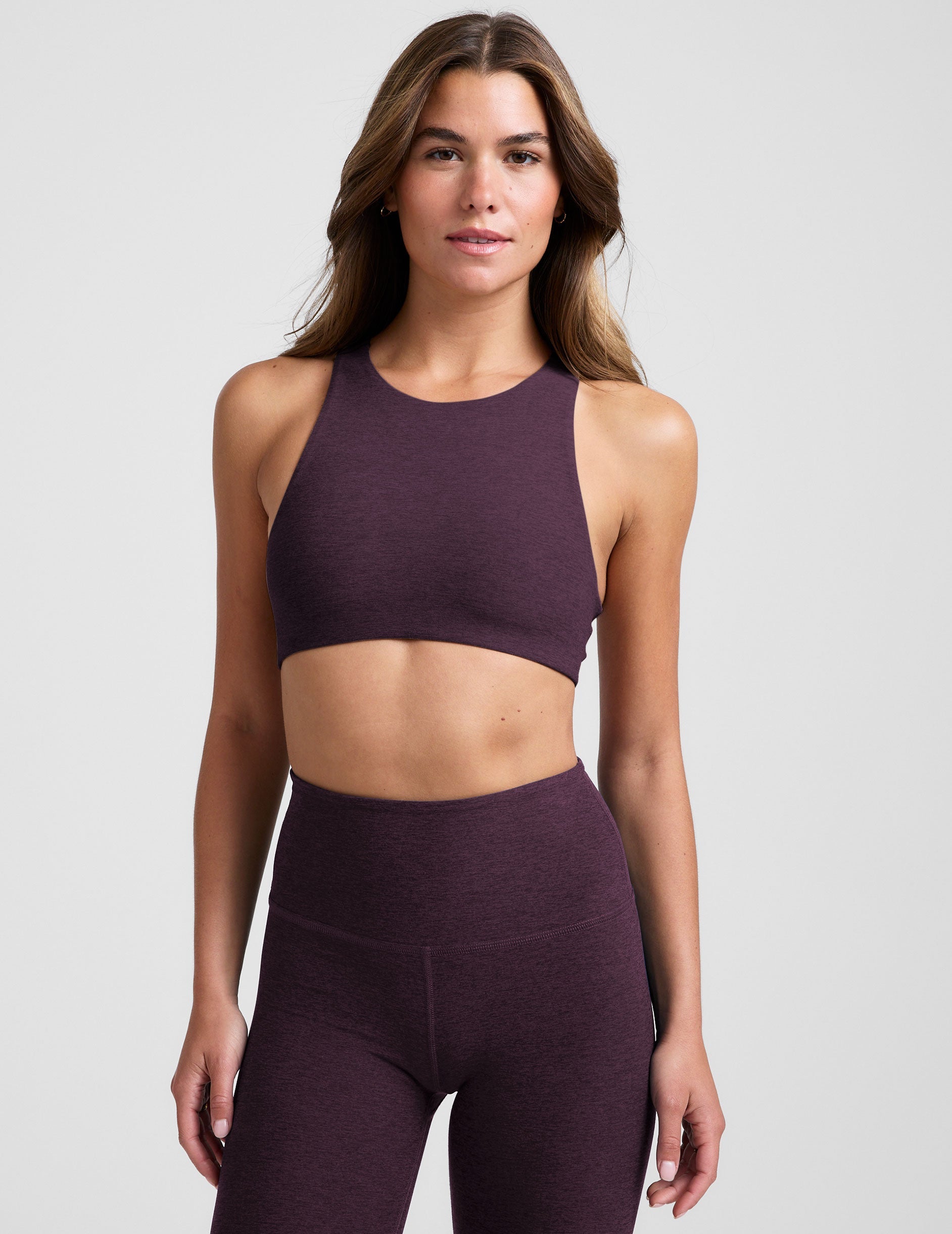 model wearing a purple high-neck racerback bra and leggings on a light gray background.