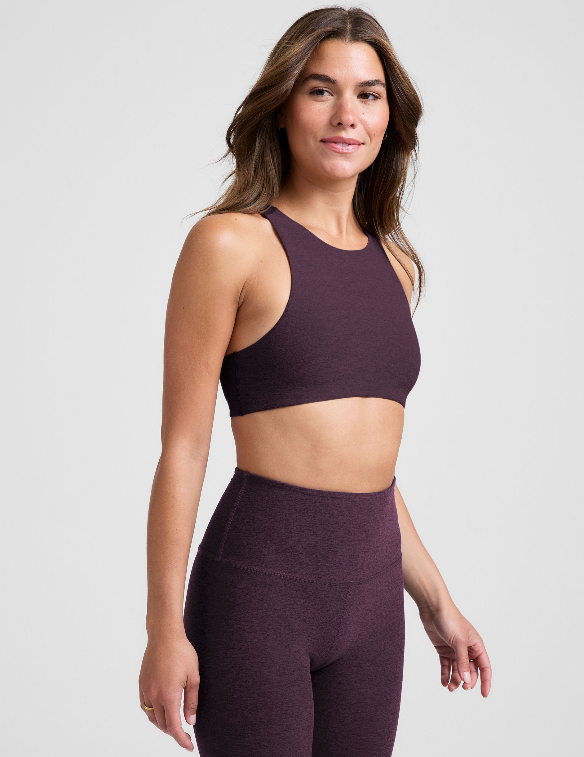 model wearing a purple high-neck racerback bra and leggings on a light gray background.