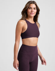 model wearing a purple high-neck racerback bra and leggings on a light gray background.
