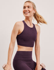 woman wearing a purple high neck bra and leggings against a plain background.