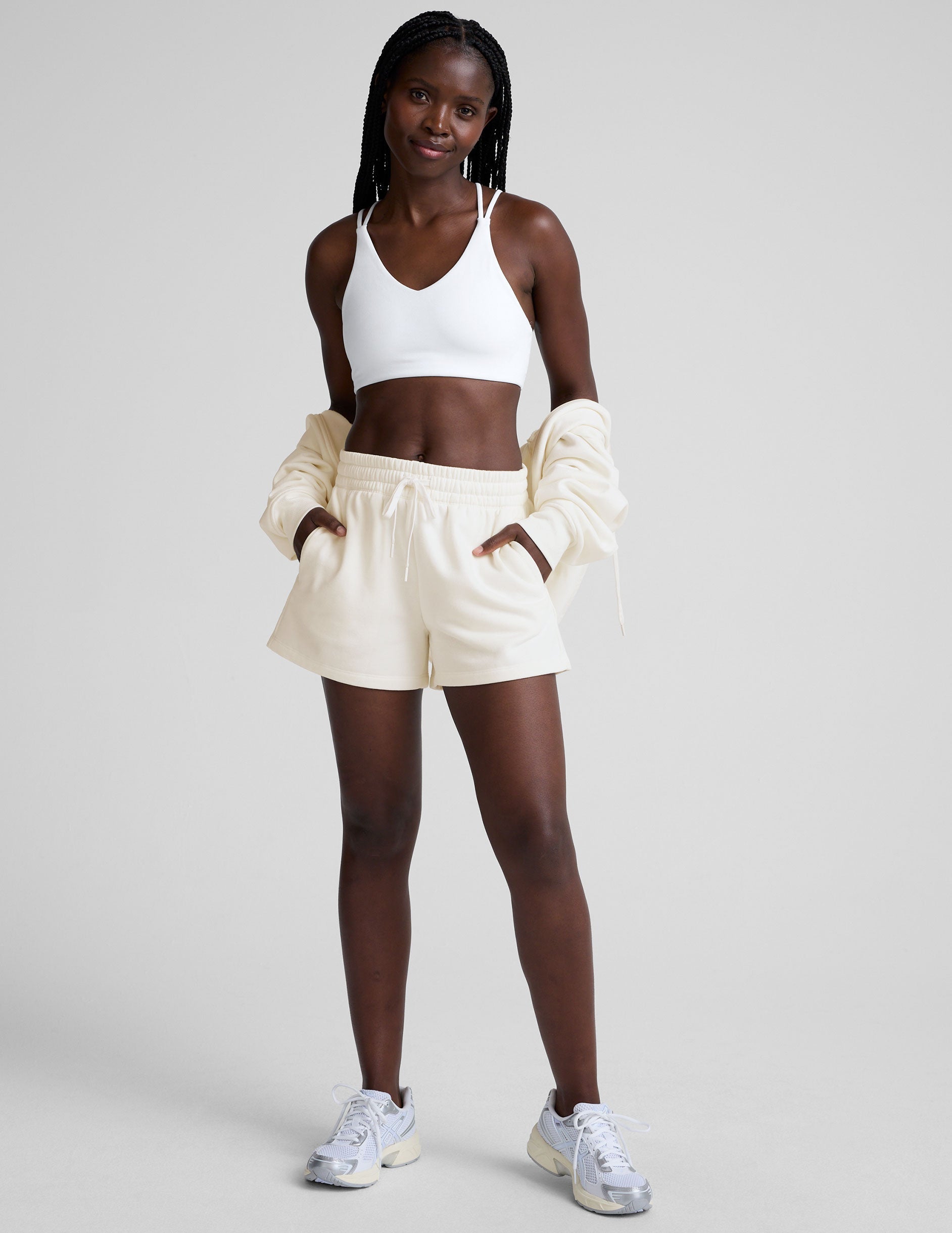woman wearing a white bra with back crossover straps and white fleece shorts against a plain background.