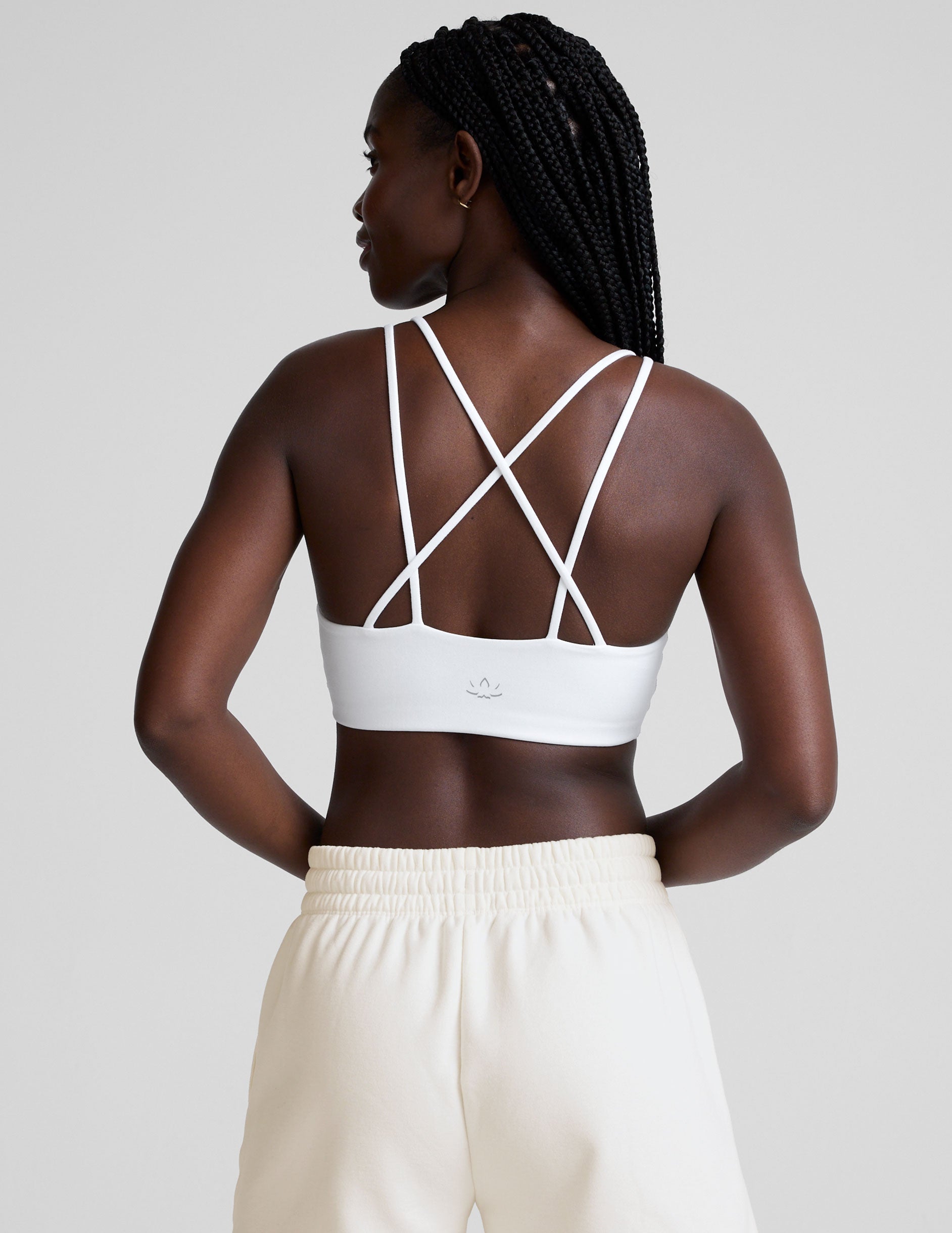 woman wearing a white bra with back crossover straps and white fleece shorts against a plain background.