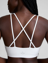 woman wearing a white bra with back crossover straps and white fleece shorts against a plain background.