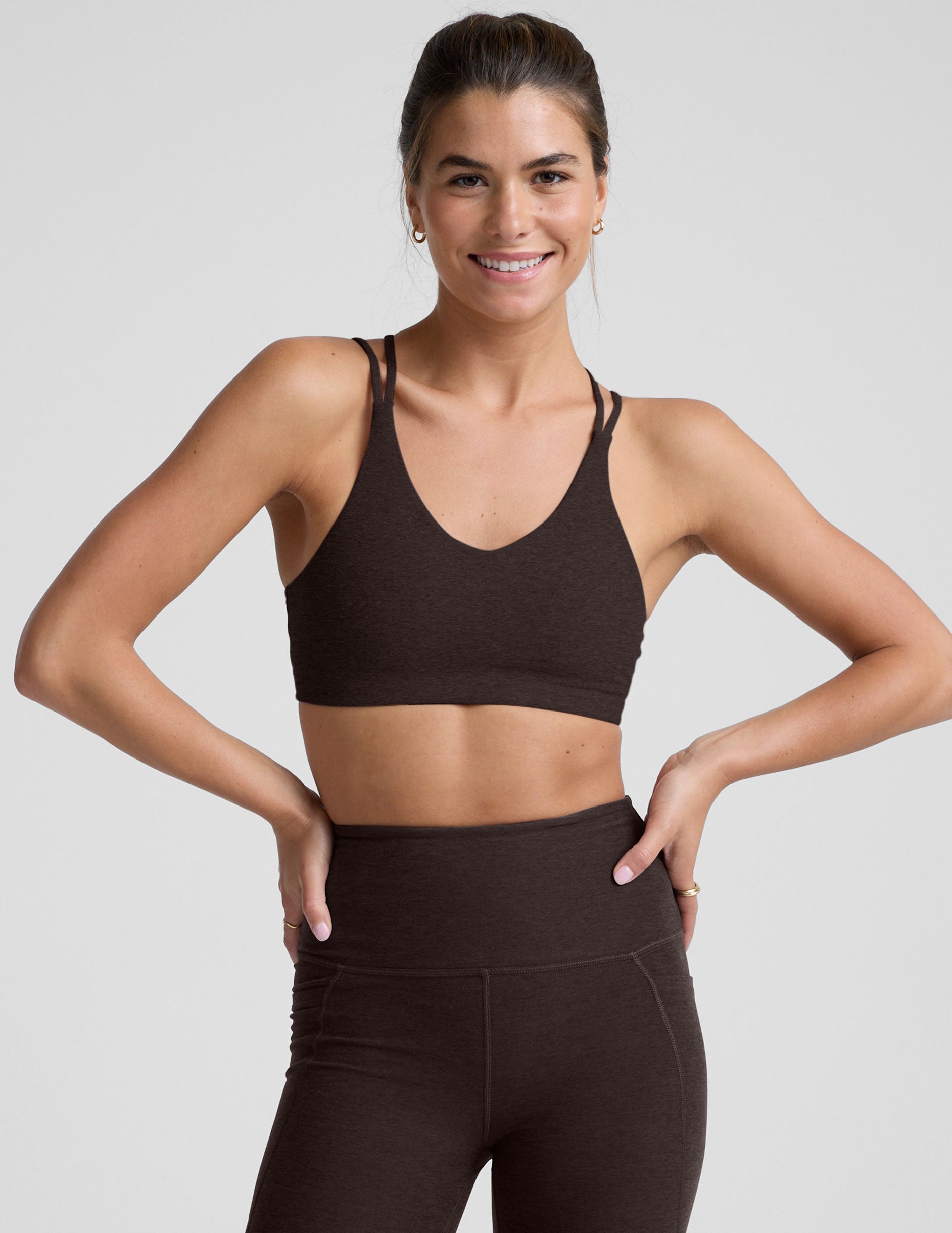 woman wearing a brown sports bra and leggings on a plain background.