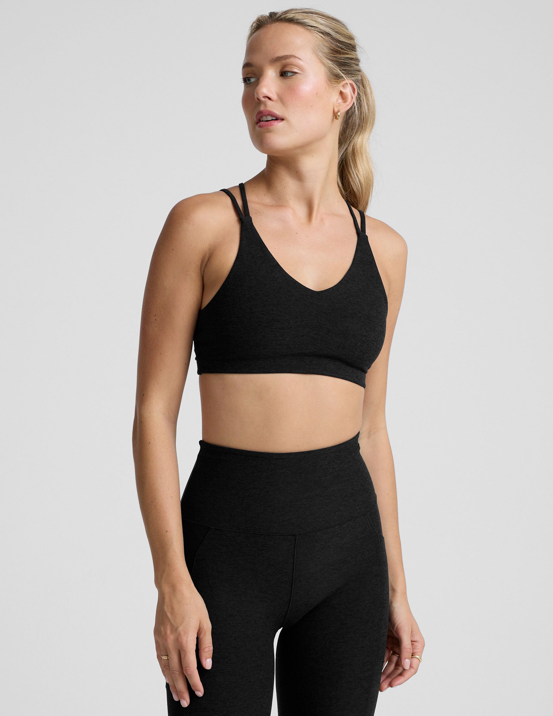 woman wearing a black sports bra with back crossover straps and leggings on a plain background.