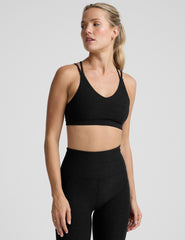woman wearing a black sports bra with back crossover straps and leggings on a plain background.