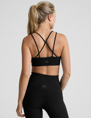 woman wearing a black sports bra with back crossover straps and leggings on a plain background.