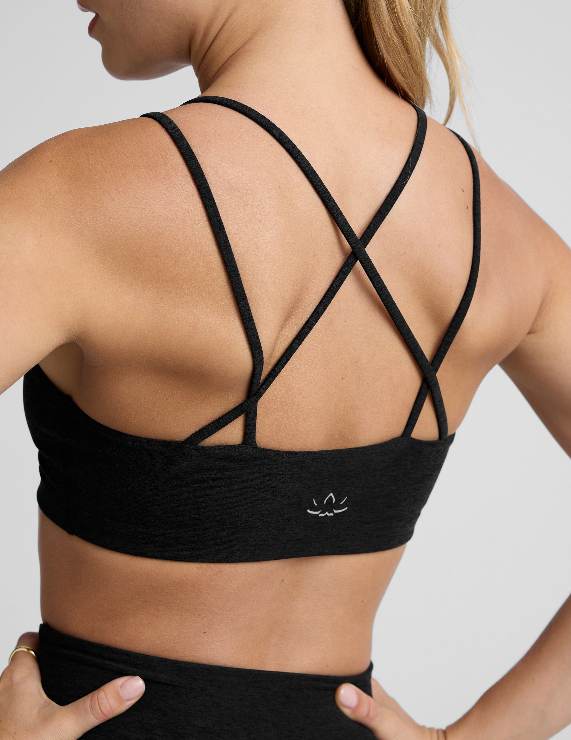 woman wearing a black sports bra with back crossover straps and leggings on a plain background.
