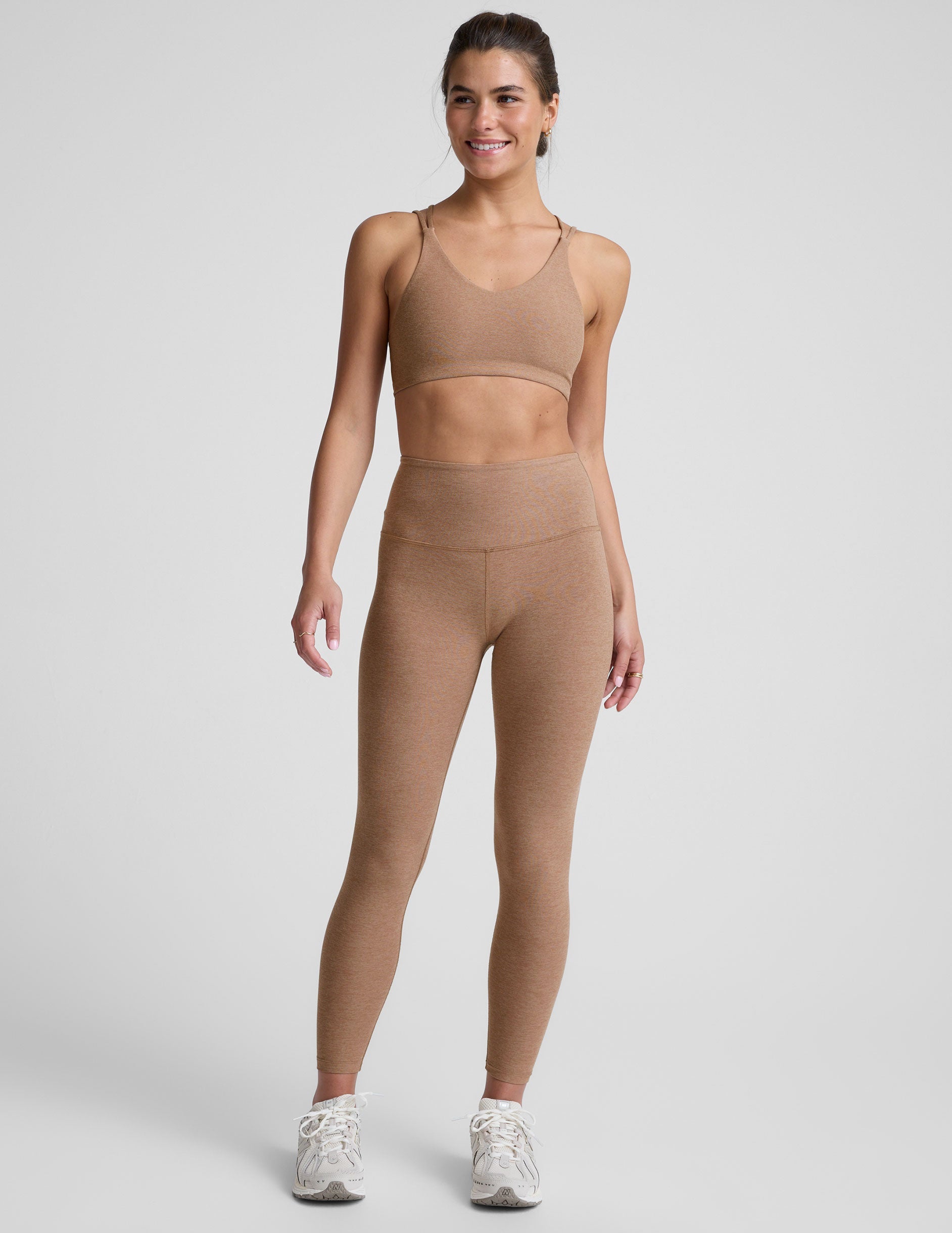 model wearing a brown sports bra with overlapping back straps and leggings on a white background.