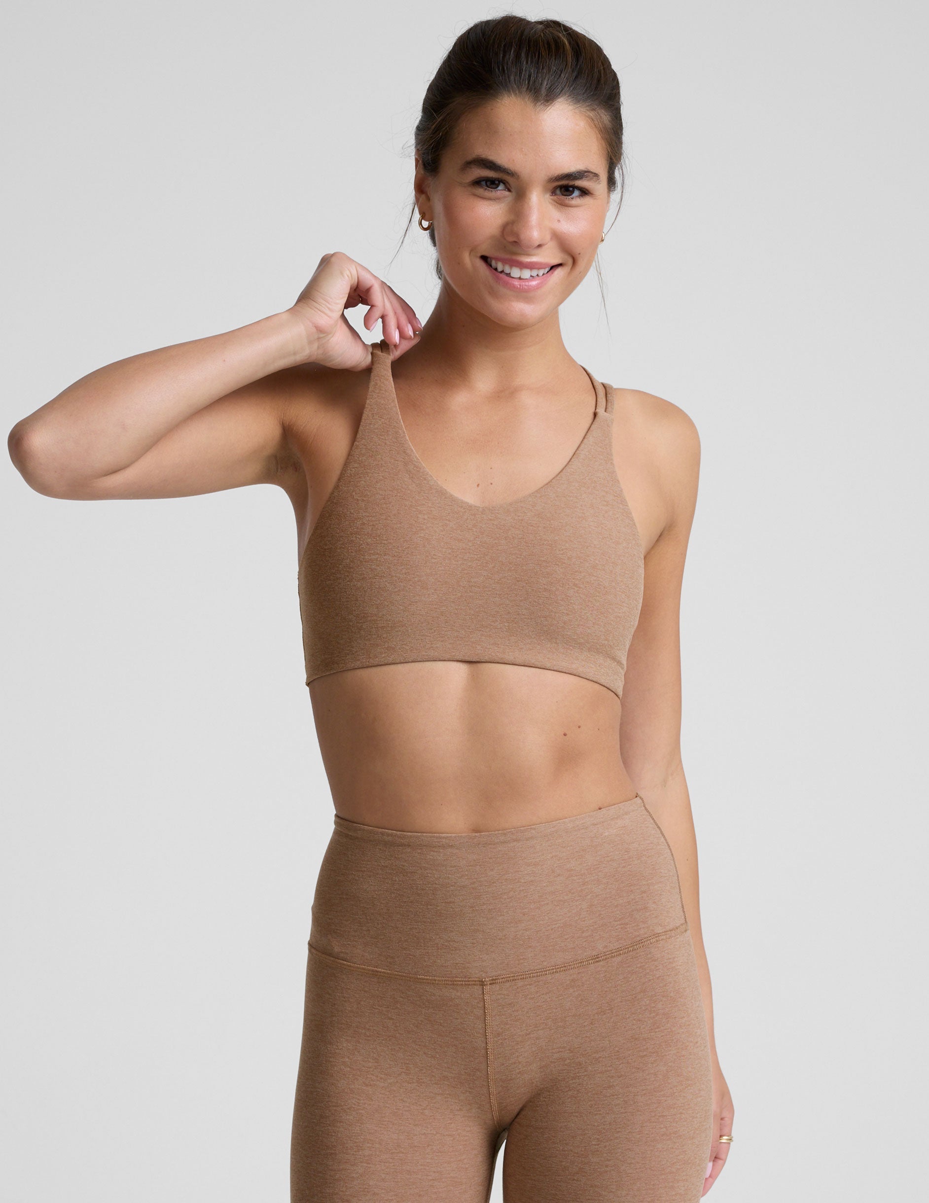 model wearing a brown sports bra with overlapping back straps and leggings on a white background.