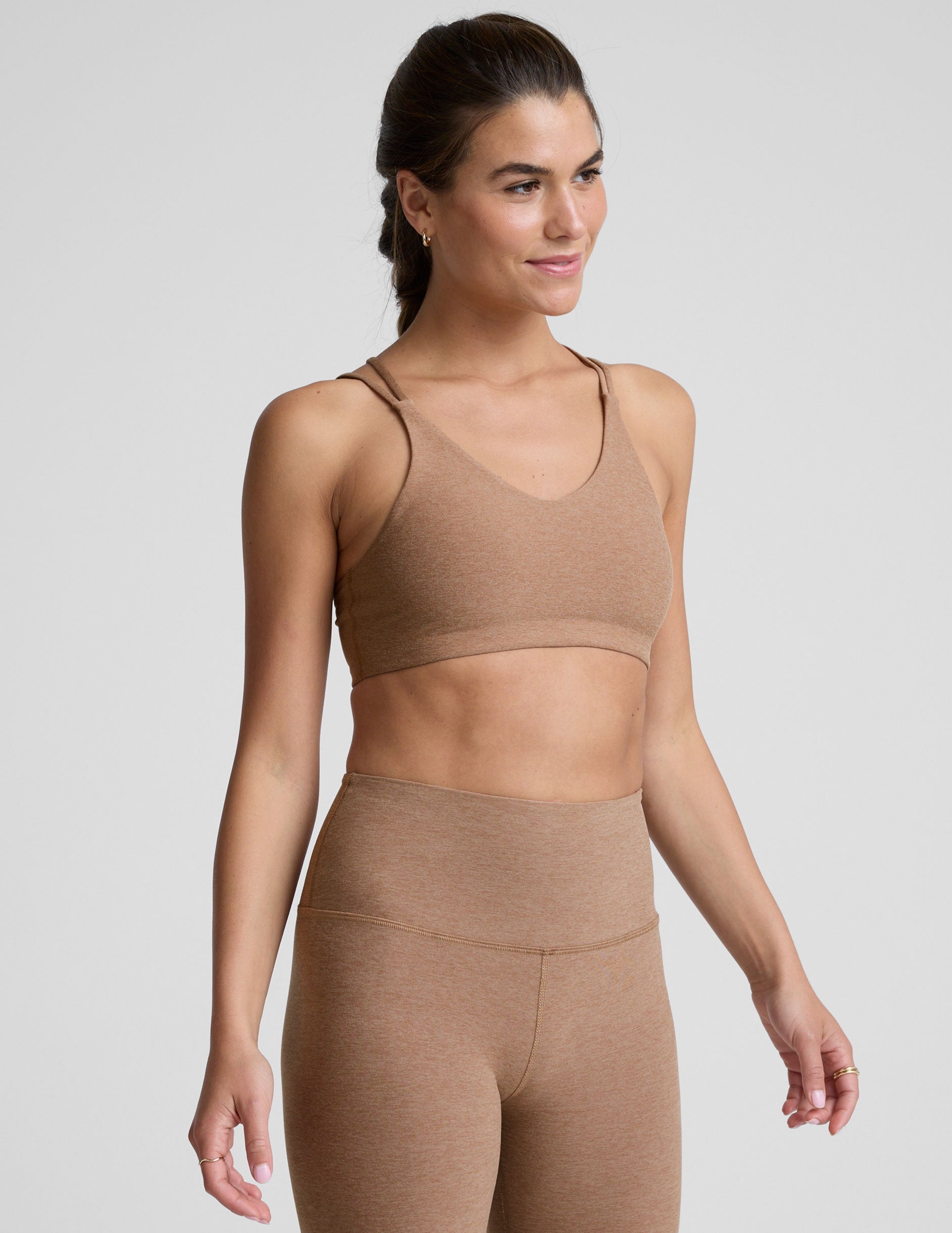 model wearing a brown sports bra with overlapping back straps and leggings on a white background.