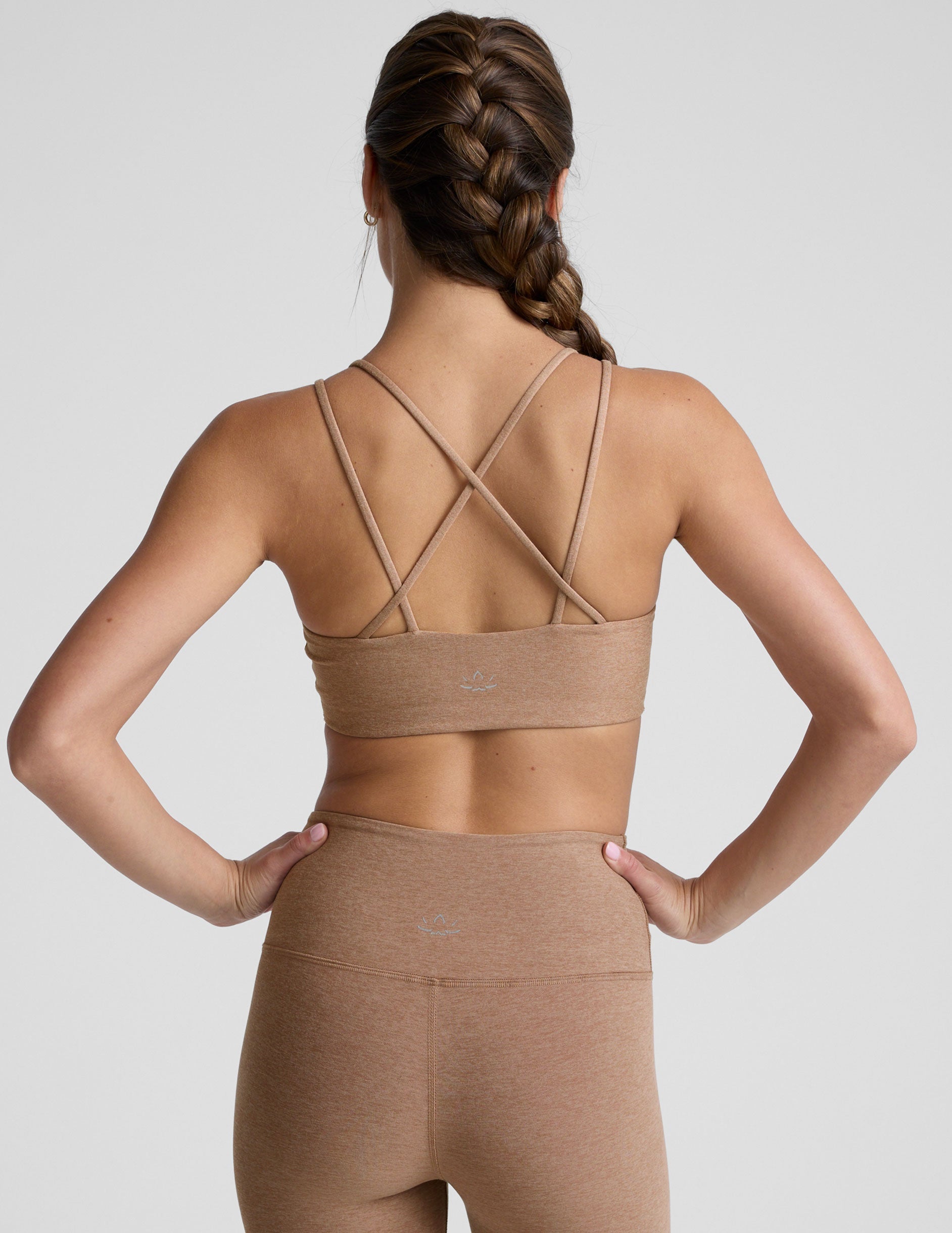 model wearing a brown sports bra with overlapping back straps and leggings on a white background.
