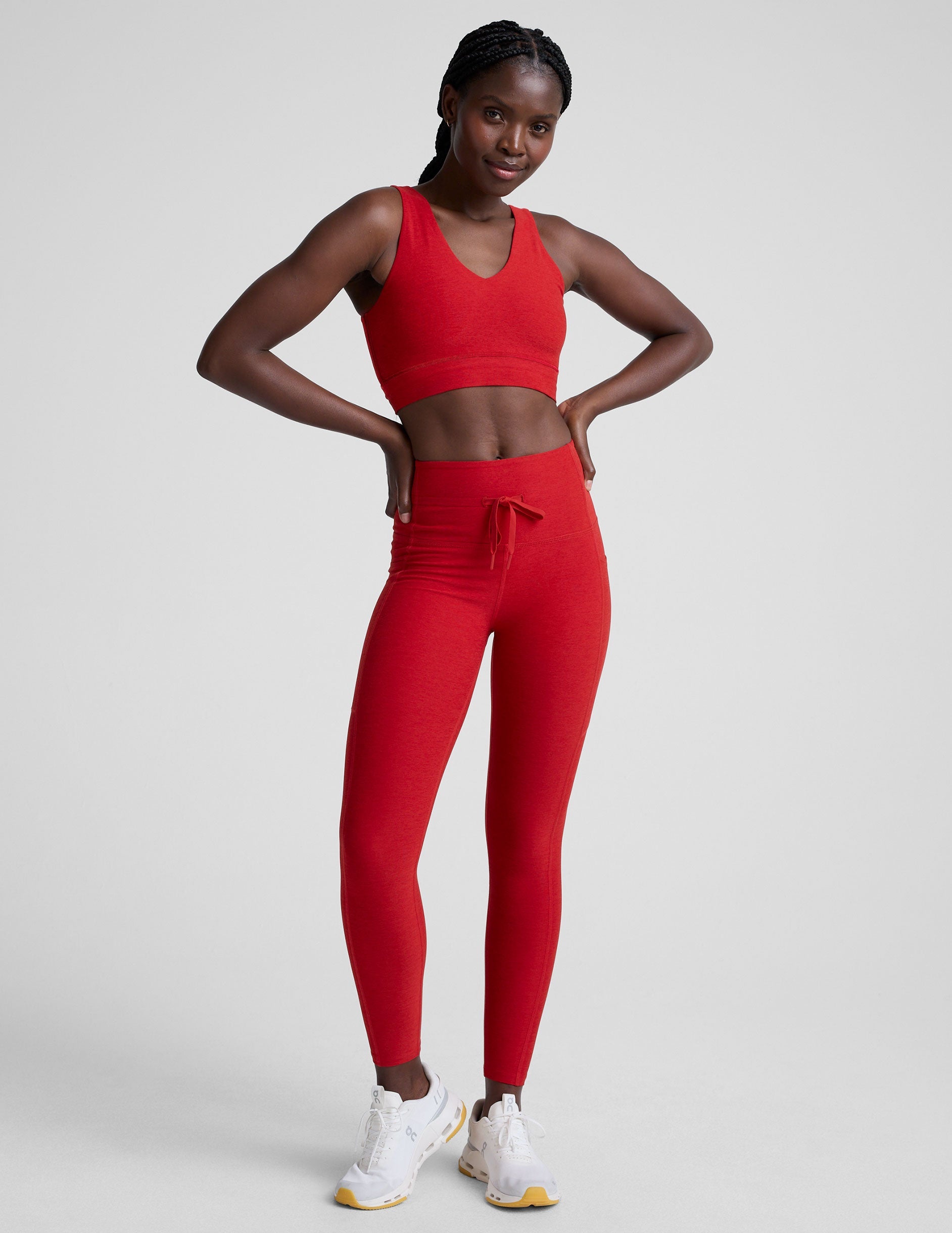 woman wearing a red v-neck long line bra and leggings on a plain background.