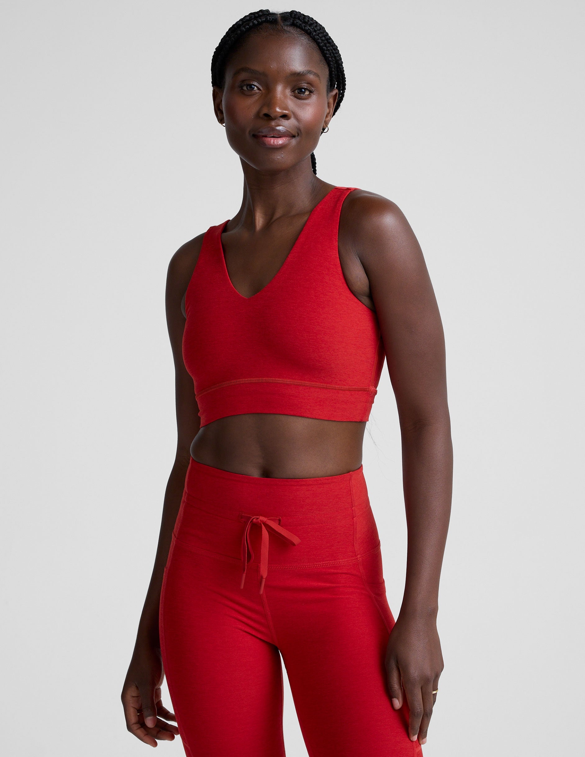 woman wearing a red v-neck long line bra and leggings on a plain background.