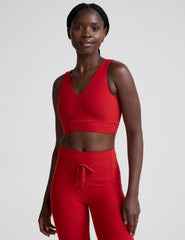 woman wearing a red v-neck long line bra and leggings on a plain background.