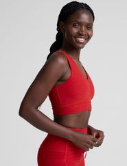 woman wearing a red v-neck long line bra and leggings on a plain background.