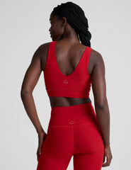 woman wearing a red v-neck long line bra and leggings on a plain background.