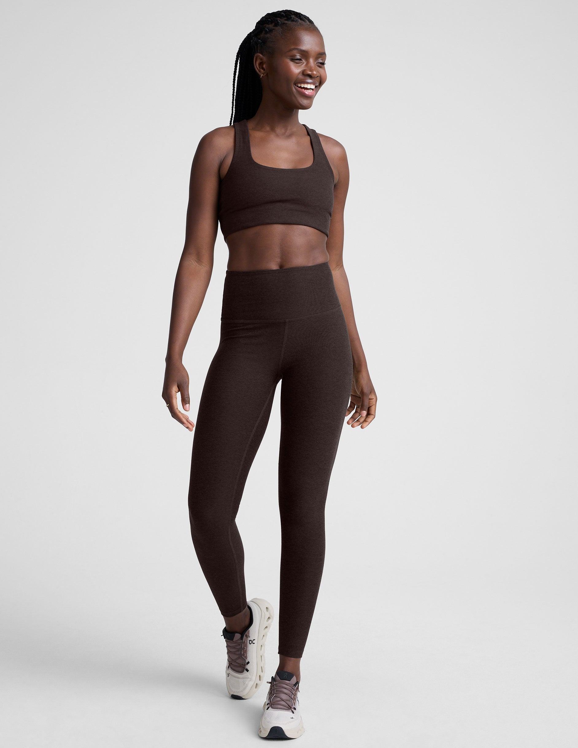 woman wearing a brown racerback bra and leggings on a plain background.