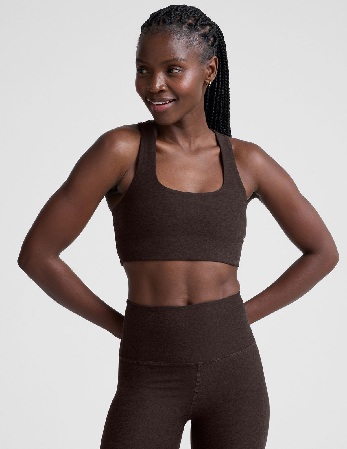 woman wearing a brown racerback bra and leggings on a plain background.