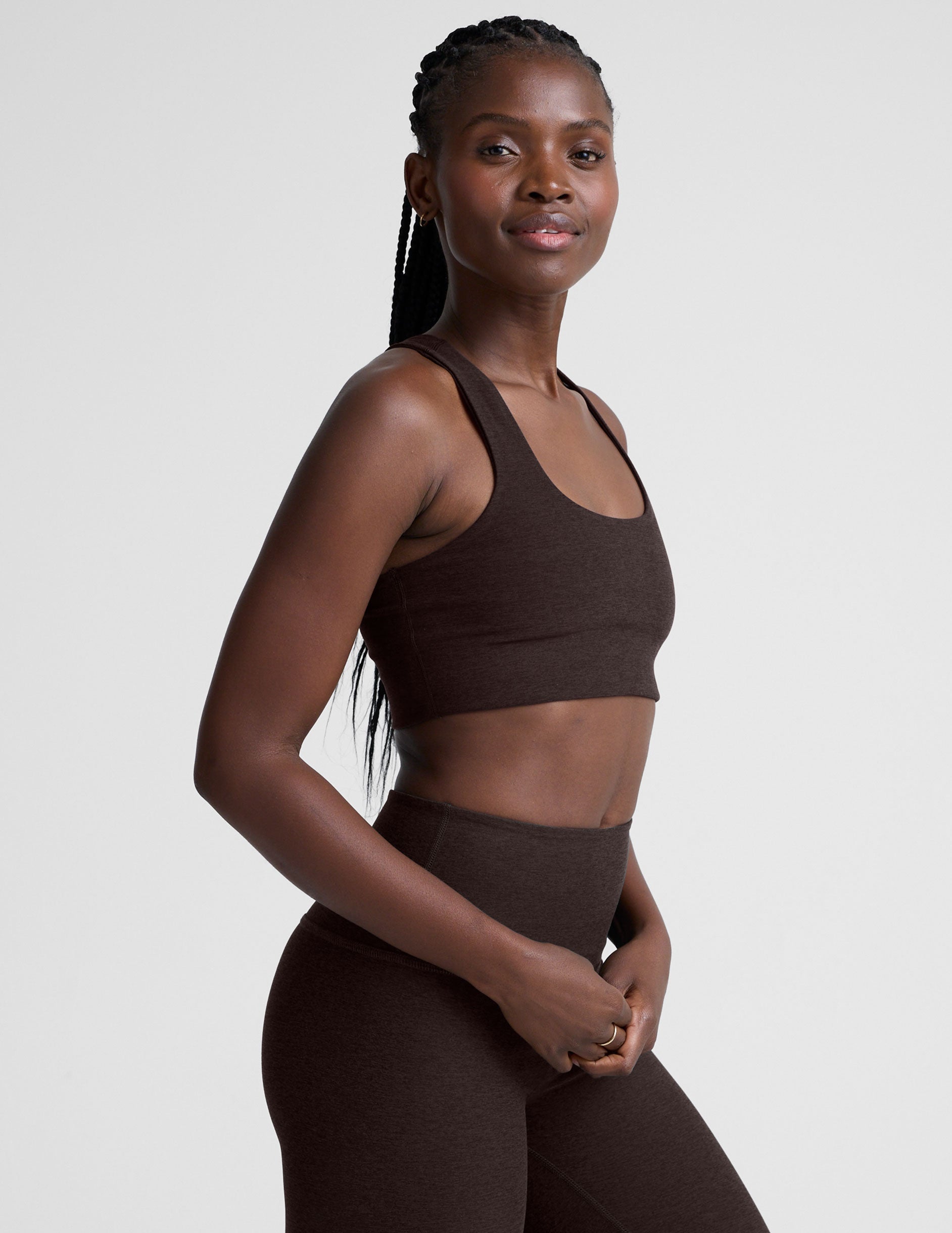 woman wearing a brown racerback bra and leggings on a plain background.